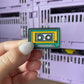 Cute Cassette Retro Enamel Pin - A charming enamel pin featuring a cute and smiling cassette tape, perfect for music lovers and fans of all things retro.