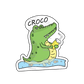 Joyful crocodile surrounded by cute fishes, holding a drink sticker, embracing a moment of happiness